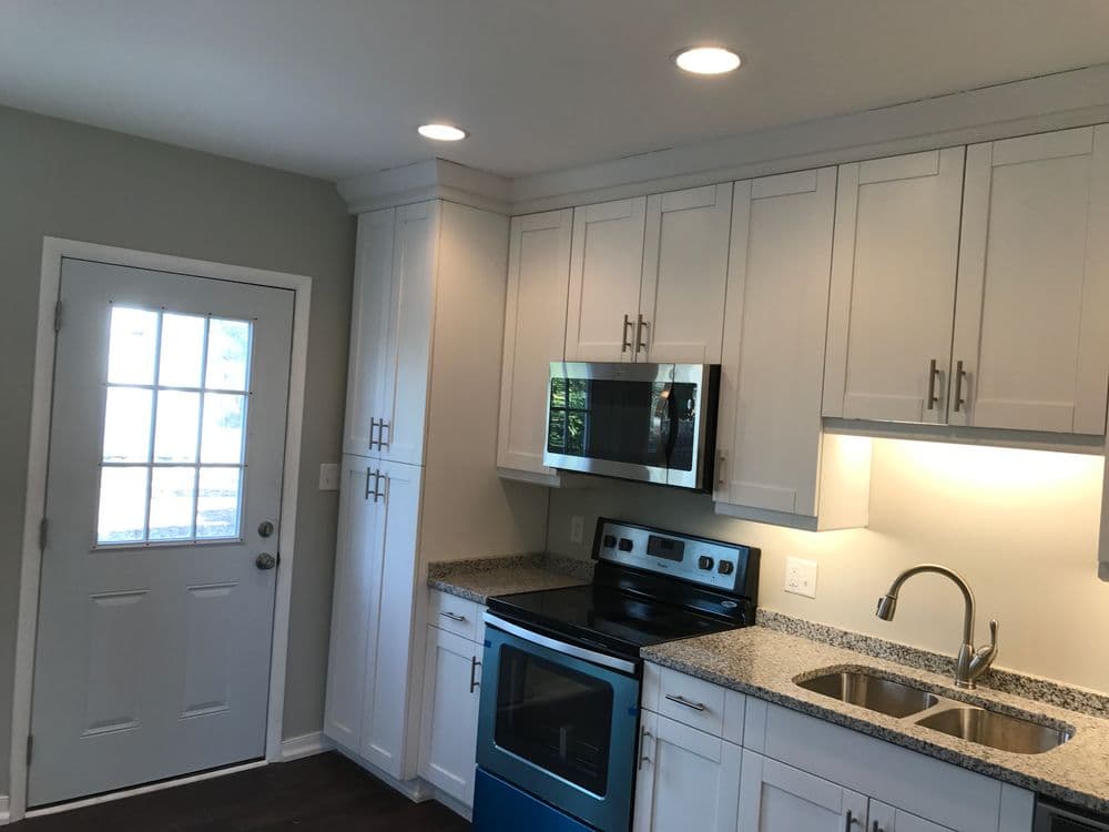 Modern kitchen with white cabinetry, granite counters, stainless steel appliances, and a door.