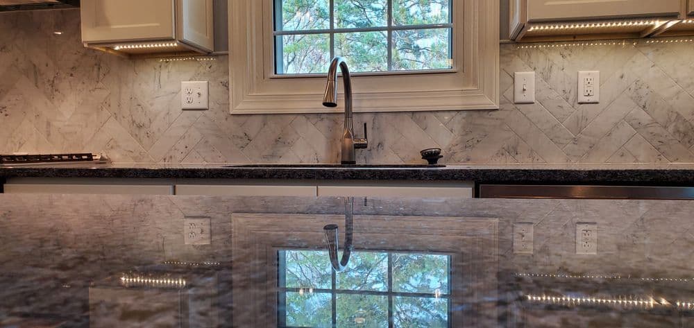 Modern kitchen with marble backsplash, sleek faucet, and reflective countertop. Natural light shines in.