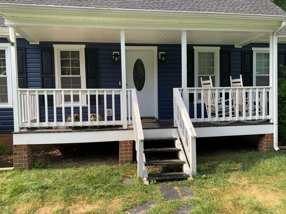 Blue house exterior with white trim, front porch, and rocking chairs on a sunny day.