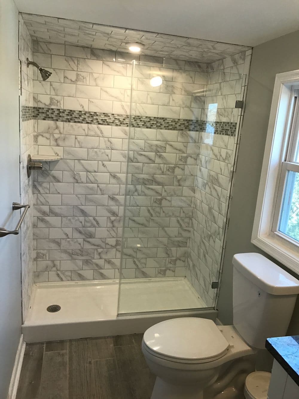 Modern bathroom with glass shower, marble tile, and elegant decor. Bright natural light illuminates space.