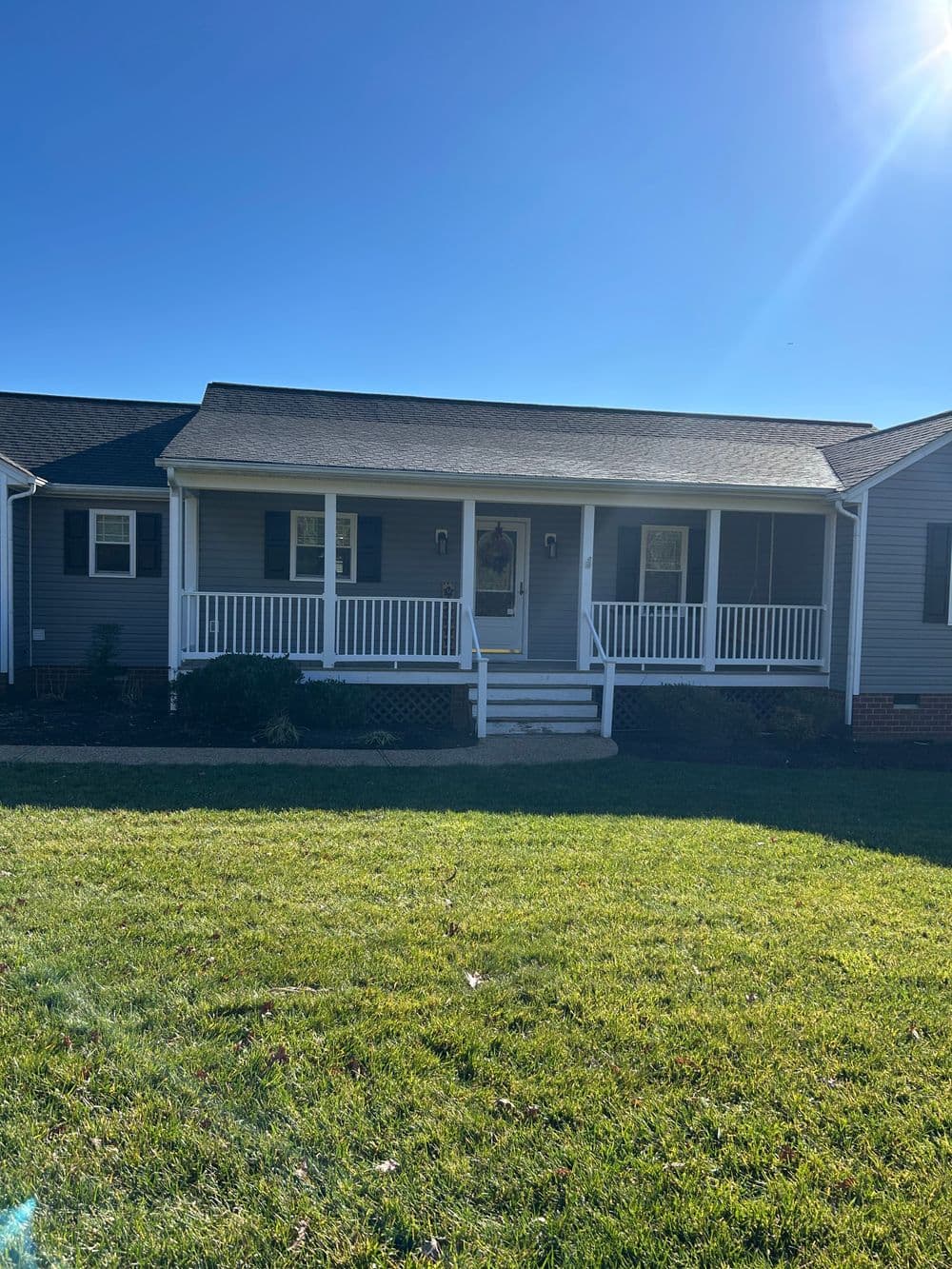 Front view of a gray house with a porch, green lawn, and clear blue sky.