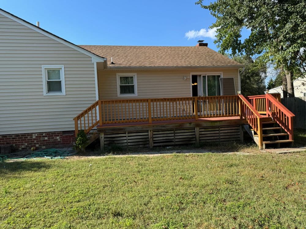 Single-story house with a wooden deck and grassy yard under a blue sky.