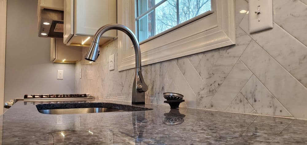 Modern kitchen sink with marble backsplash and sleek faucet in bright natural light.
