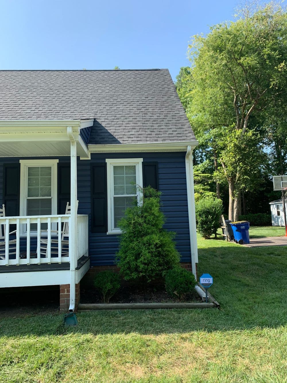Blue house with white porch steps and green landscaping in bright sunlight.