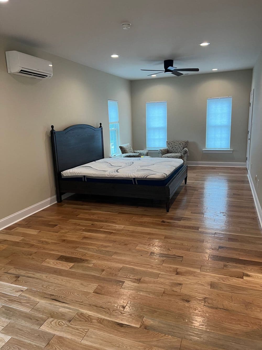 Spacious bedroom with hardwood floors, a dark wood bed, and natural light from windows.